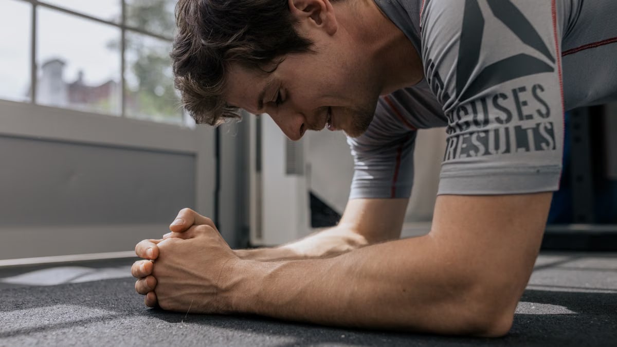Focused man doing a plank exercise inside a gym for a core workout.